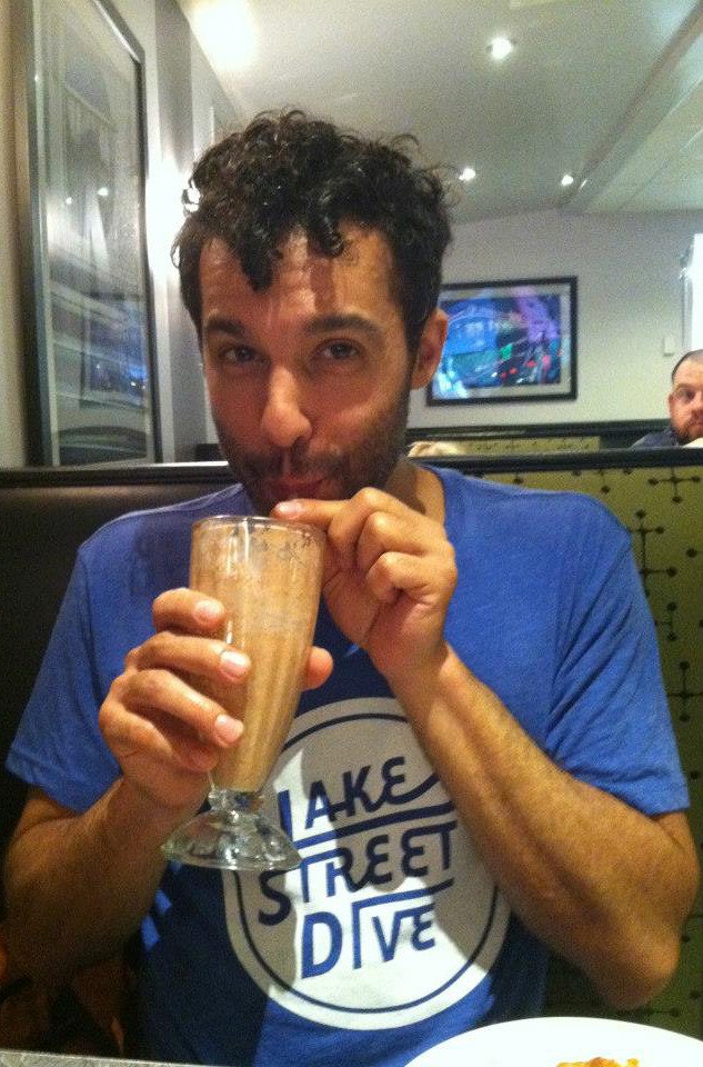 Justin in a booth at Veggie Galaxy wearing his Lake Street Dive shirt and drinking a chocolate coconut-milk shake.